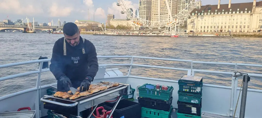 Thames boat party catering: Route Catering chef grilling a live BBQ on a boat with the London Eye behind