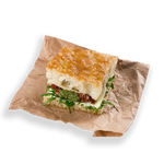 Sandwich with greens and cheese on brown paper against a white background