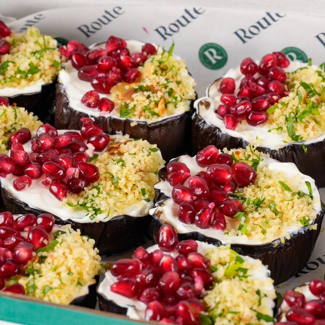 Close-up of aubergine discs topped with spiced bulgur, pomegranate seeds and yogurt - Route Catering