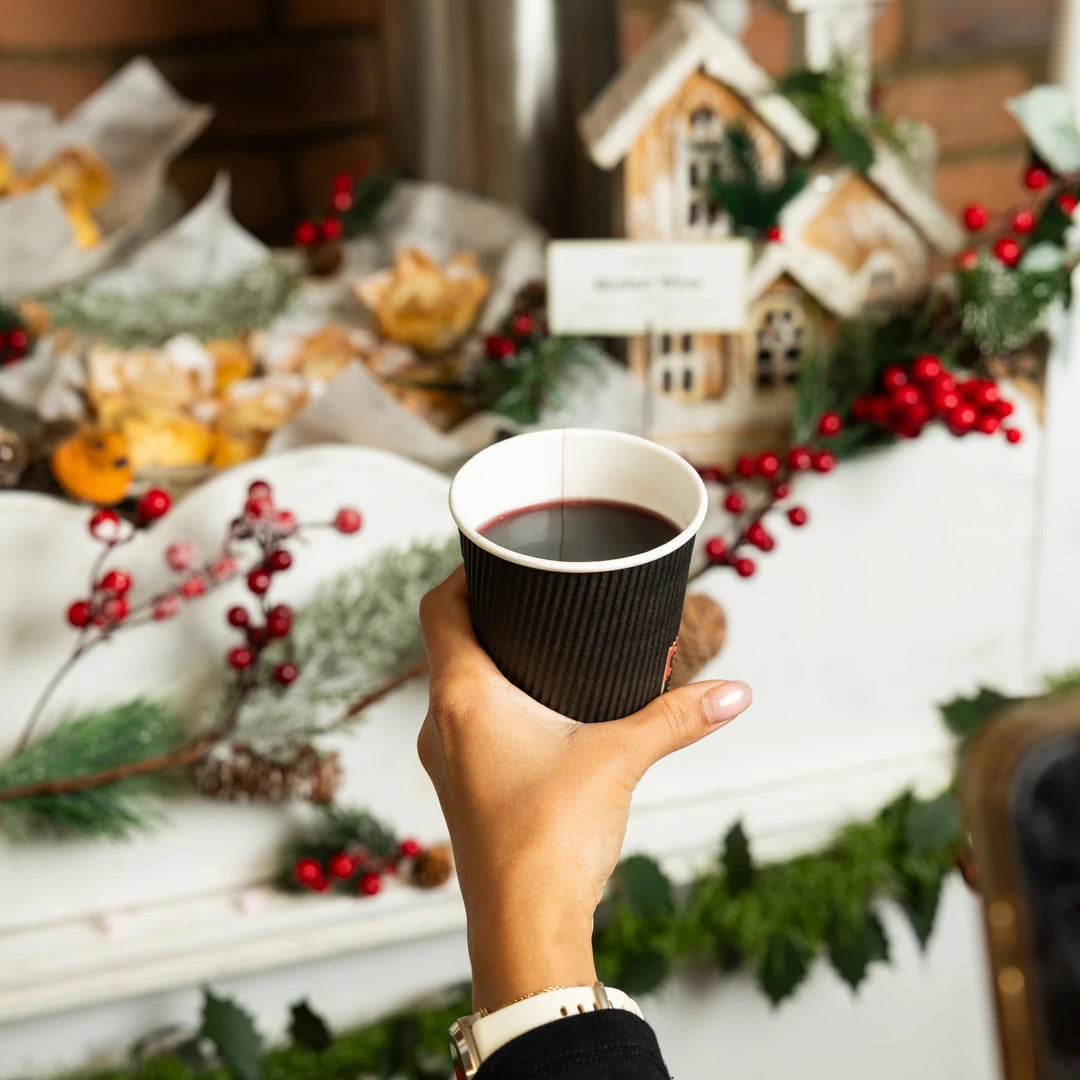 A cup of non-alcoholic mulled wine held in front of Christmas decorations - Route Catering